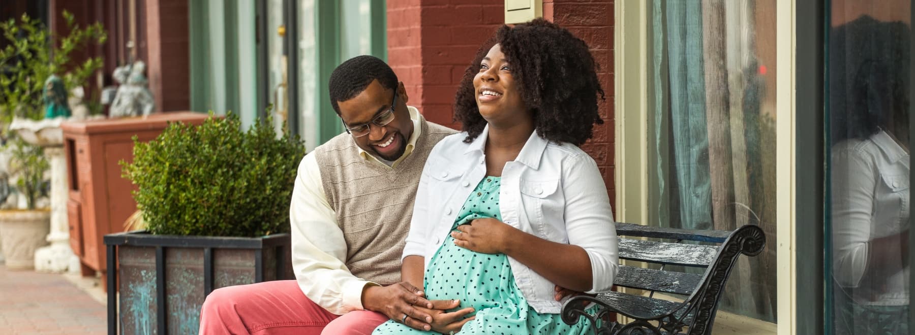 Smiling man puts hand on pregnant woman's stomach while sitting on a bench